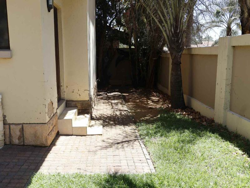 Rear exterior area featuring a paved walkway, boundary wall, and tiled steps leading to the house entrance, showing signs of weathered exterior paint.
