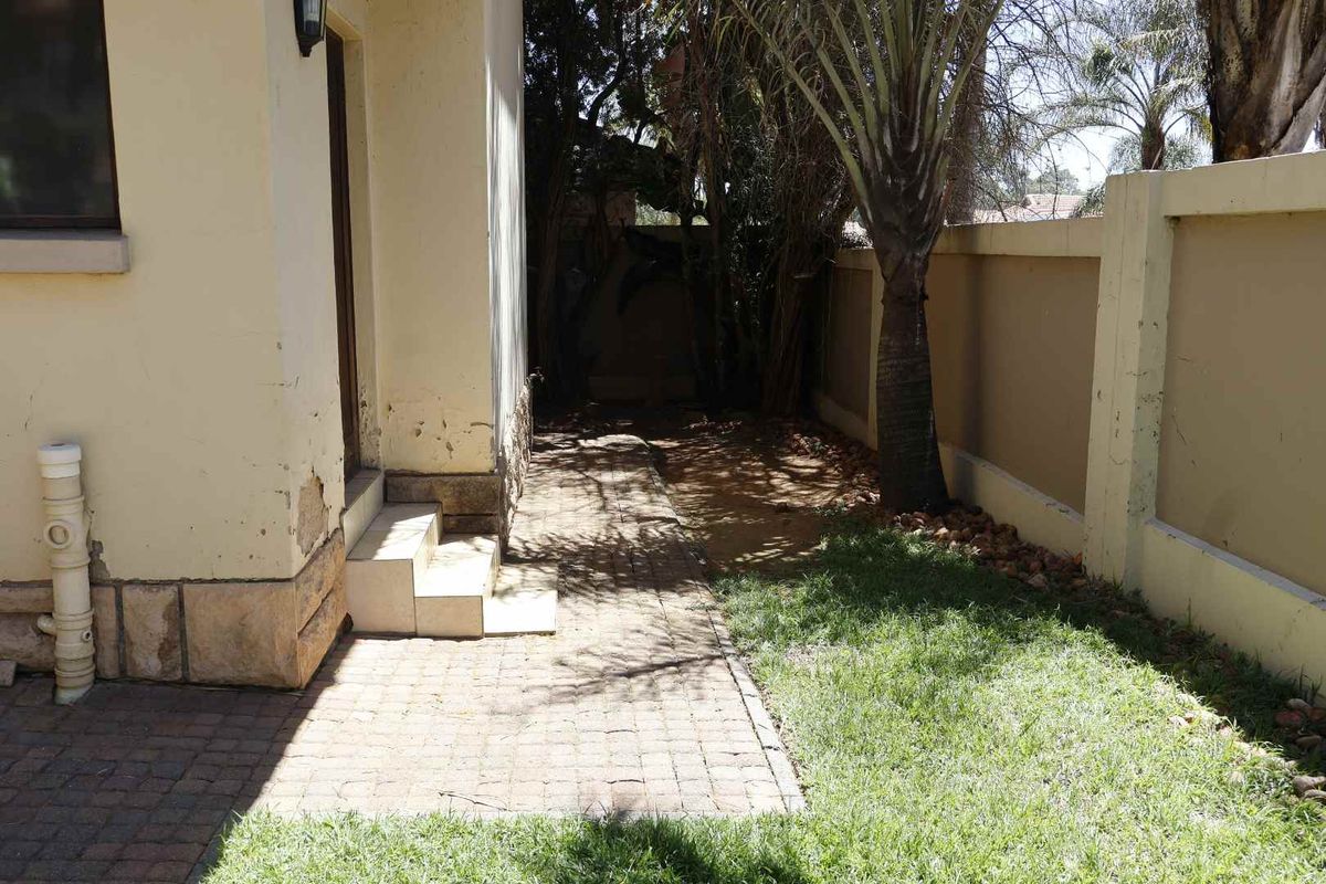 Rear exterior area featuring a paved walkway, boundary wall, and tiled steps leading to the house entrance, showing signs of weathered exterior paint.