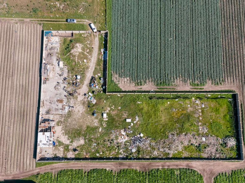 Aerial view of a vacant residential plot enclosed by a perimeter wall, featuring significant debris and overgrown vegetation.