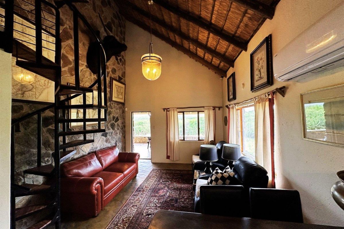 Spacious living area featuring a high vaulted thatched ceiling, exposed stone feature wall, and a striking black metal spiral staircase.