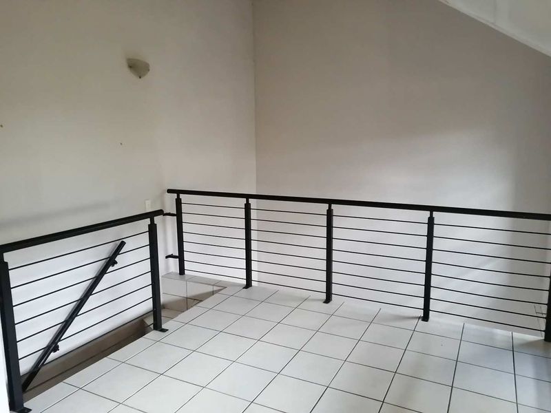 An empty landing area featuring tiled flooring and a modern black metal balustrade overlooking the staircase.