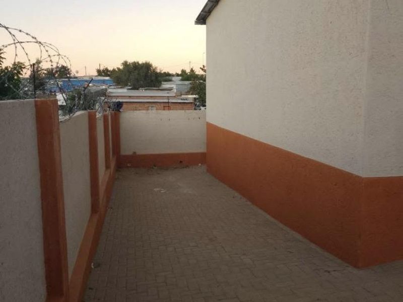 A side or rear exterior walkway featuring paved flooring and a perimeter wall topped with security razor wire.