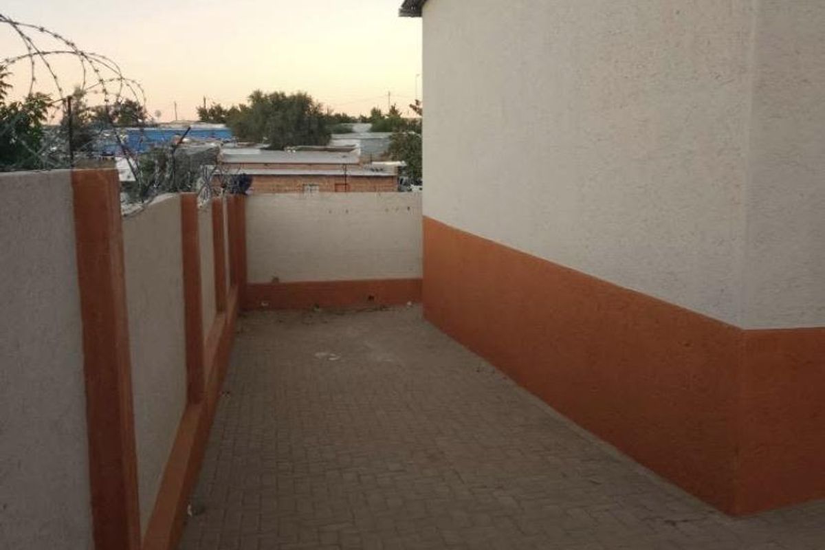 A side or rear exterior walkway featuring paved flooring and a perimeter wall topped with security razor wire.