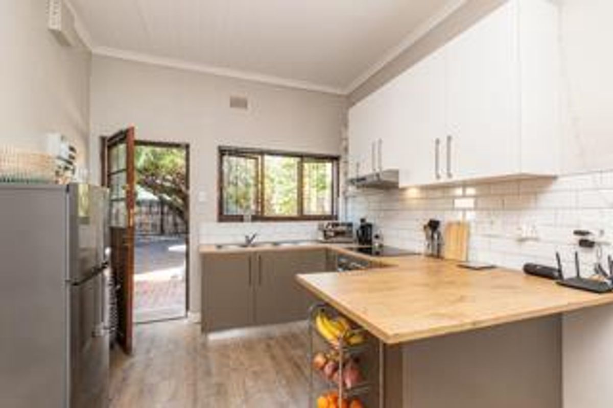 A functional kitchen featuring modern white upper cabinetry, wood-tone countertops, subway tile backsplash, and direct access to the exterior via a security door.