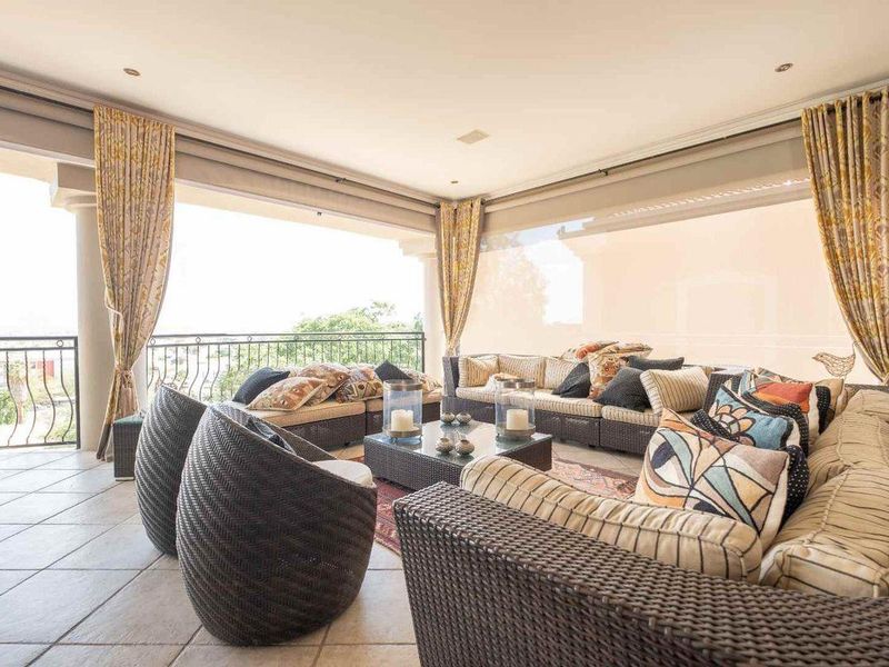 A spacious covered patio featuring tiled flooring, wrought iron balustrades, and retractable outdoor blinds, offering a comfortable area for outdoor relaxation.