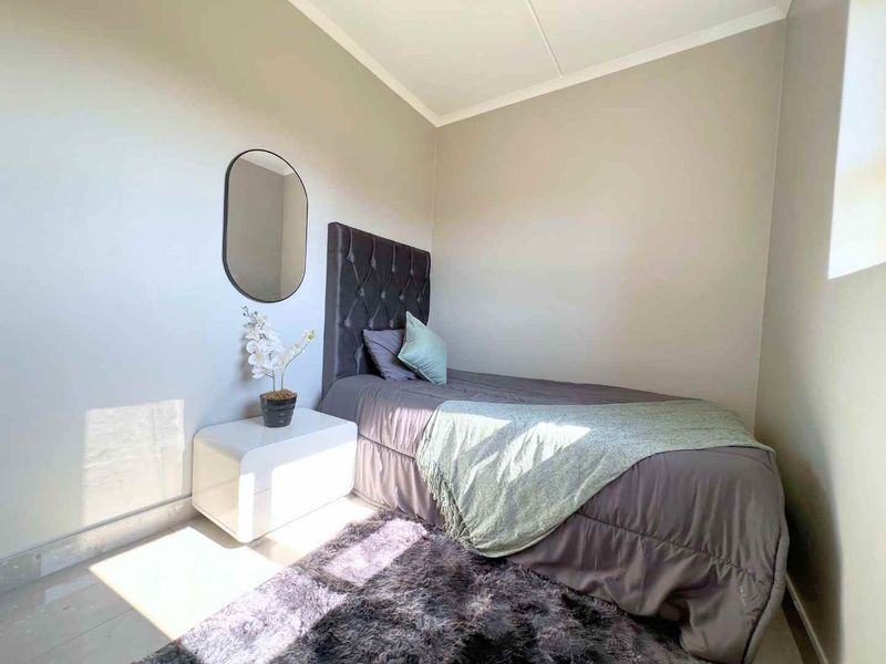 A well-lit bedroom featuring neutral wall tones, tiled flooring, and a coved ceiling, providing a clean and comfortable living space.
