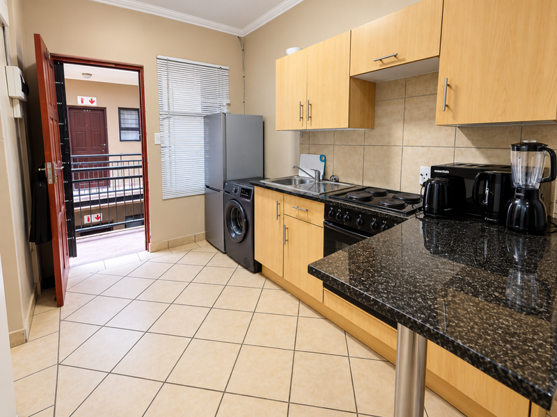 A functional kitchen featuring light wood cabinetry, granite countertops, tiled flooring, and direct access to an external walkway.