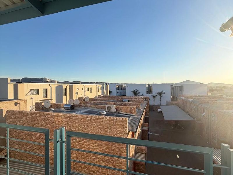 A balcony with a metal balustrade and tiled flooring, offering an elevated view over the surrounding residential complex.