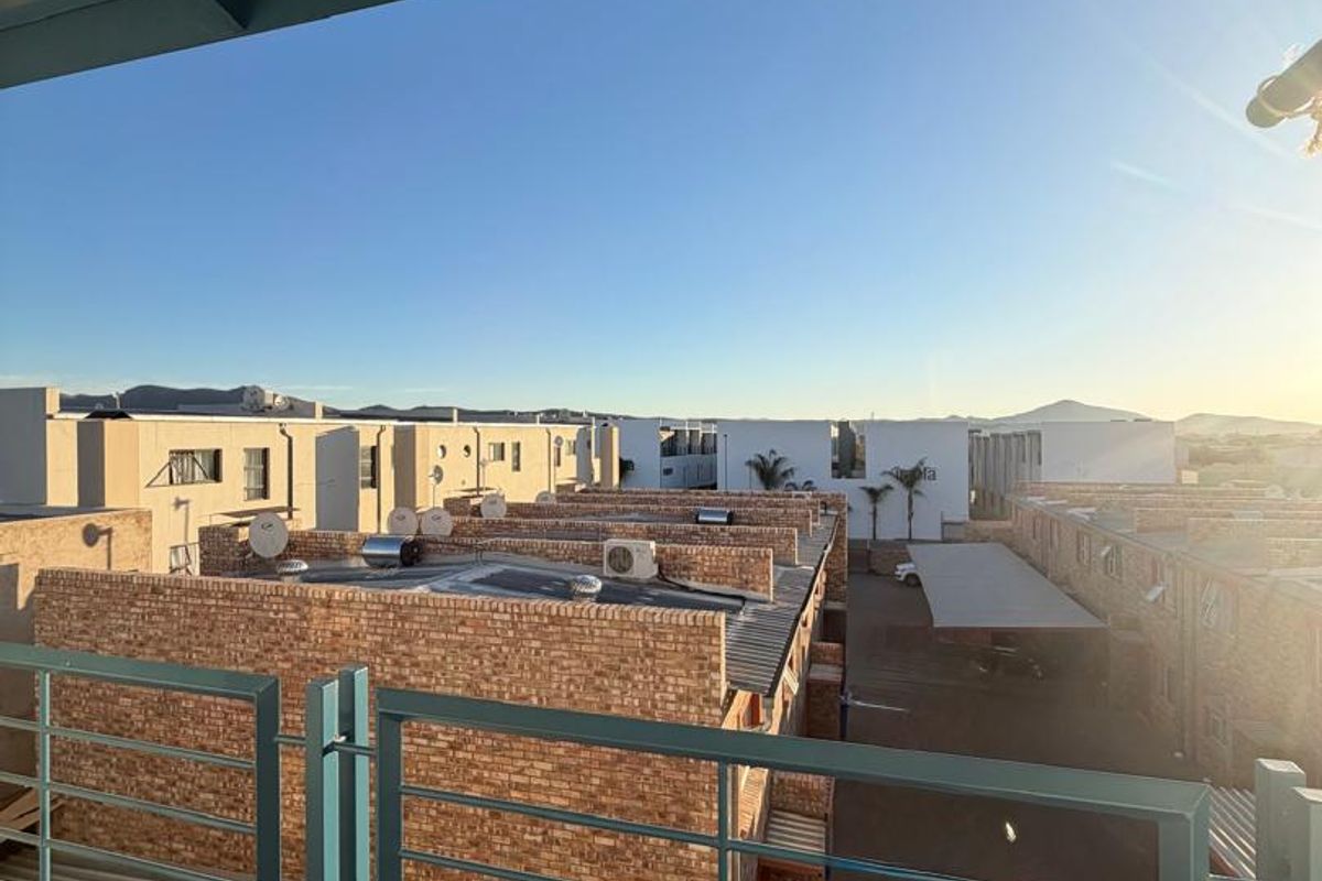 A balcony with a metal balustrade and tiled flooring, offering an elevated view over the surrounding residential complex.