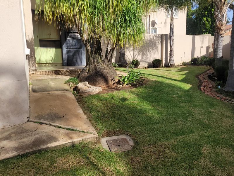 Rear garden area featuring a lawn, mature trees, a concrete pathway, and a built-in braai area against the exterior wall.