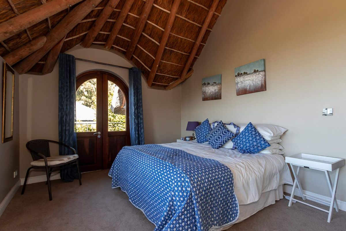 A cozy bedroom featuring a unique vaulted thatched ceiling with exposed timber rafters and an arched wooden door leading to the exterior.