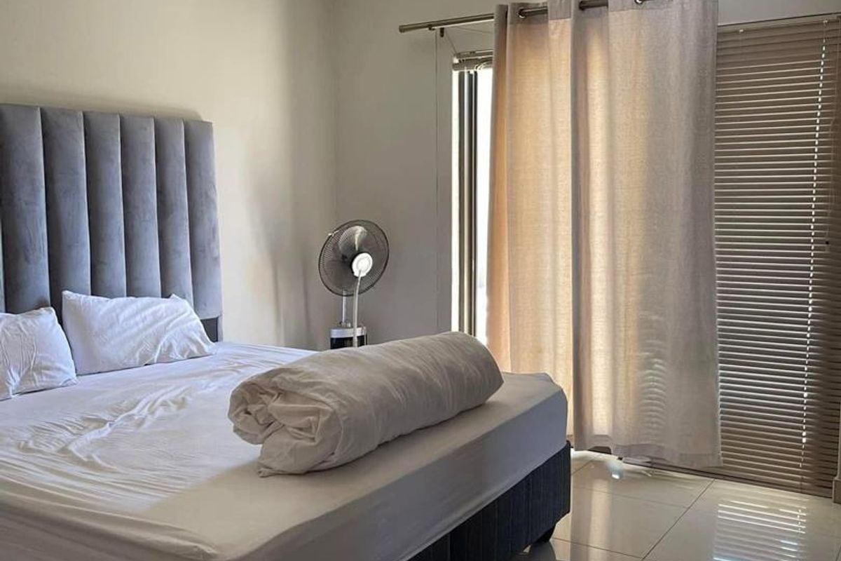 A well-lit bedroom featuring tiled flooring, neutral wall finishes, and a sliding door with integrated blinds and curtains leading to an outdoor area.