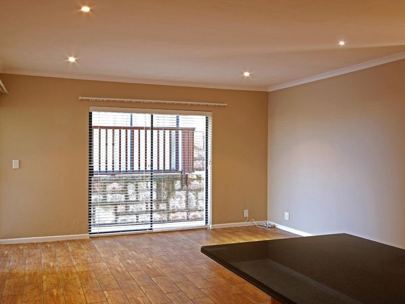 Spacious open-plan living area featuring wood-look tile flooring, recessed downlighting, and a sliding glass door leading to an outdoor balcony.