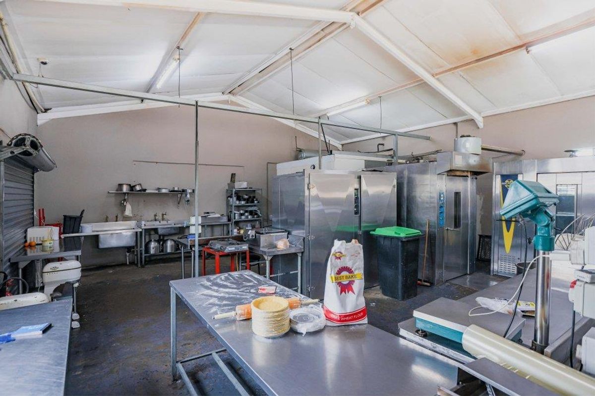 A commercial kitchen facility featuring industrial-grade stainless steel prep tables, heavy-duty ovens, and a functional wash-up area with exposed structural ceiling beams.