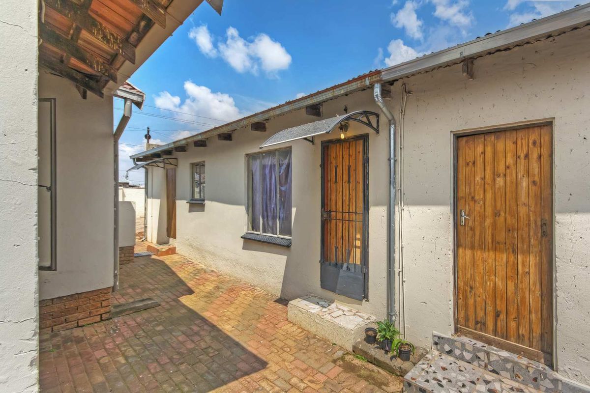 Exterior view of the property showing a paved courtyard area with access to multiple entry points and basic structural finishes.