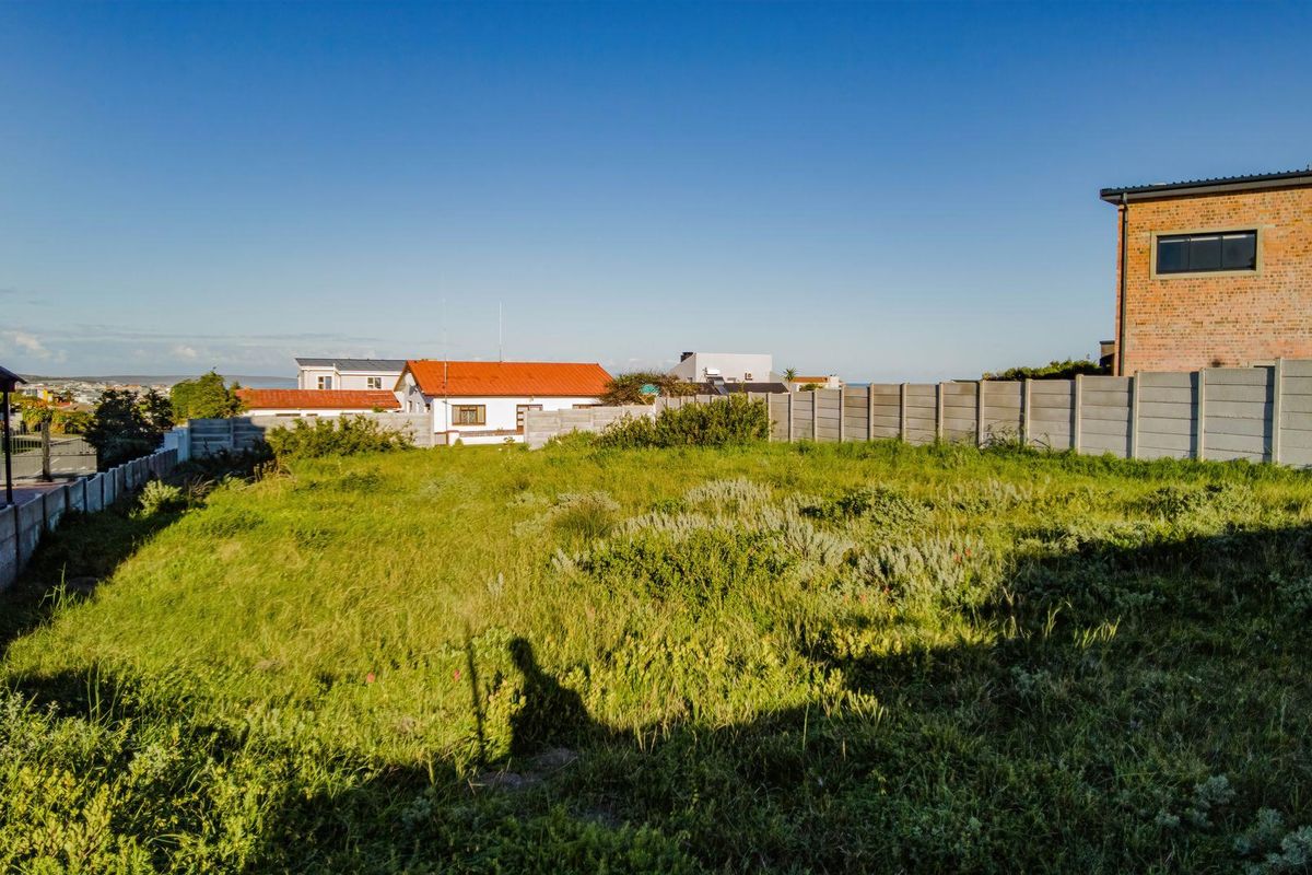 A vacant residential plot featuring overgrown grass and enclosed by precast concrete boundary walls, situated in a developed neighborhood.