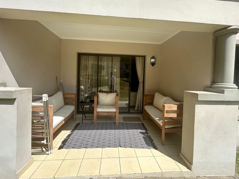 A covered patio area featuring tiled flooring, concrete pillars, and a sliding glass door providing access to the interior living space.