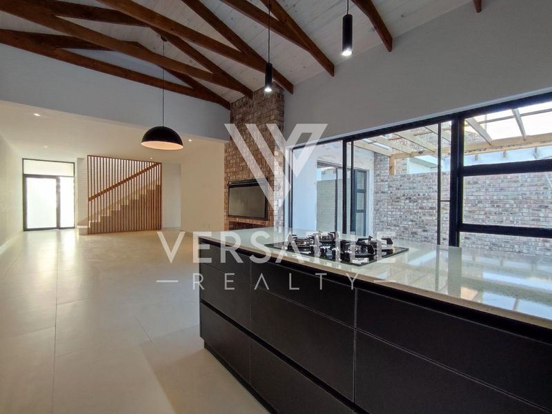 Spacious open-plan living area featuring exposed timber beams, a modern kitchen island with gas hob, built-in fireplace, and seamless access to the outdoor patio.