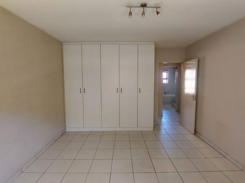 Spacious bedroom featuring neutral walls, tiled flooring, and ample built-in cupboard storage, with direct access to an adjoining bathroom.