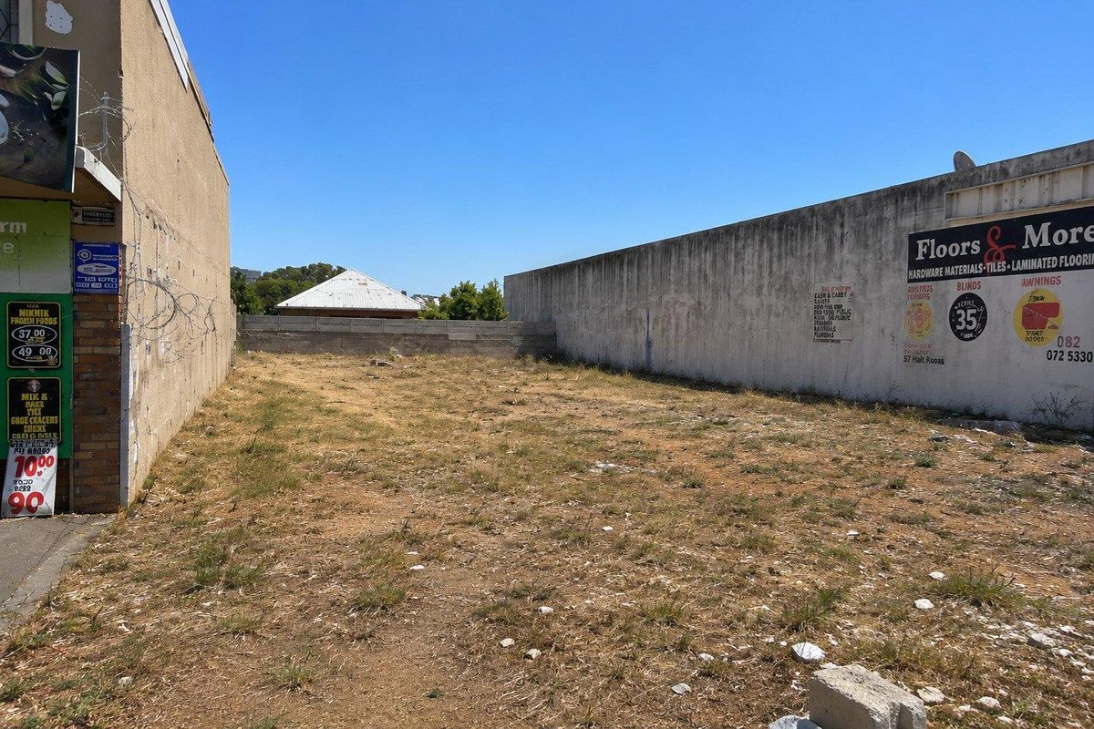 A vacant commercial land plot enclosed by high boundary walls with existing signage and razor wire security.