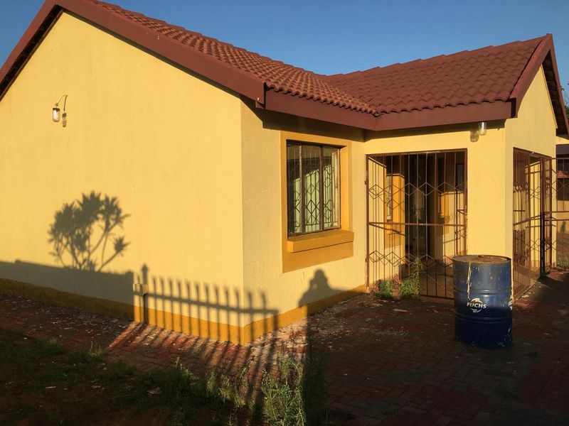 Rear exterior view of a single-story house featuring a tiled roof, paved patio area, and security gates on the entrance and windows.