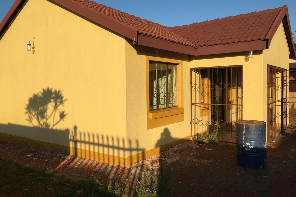 Rear exterior view of a single-story house featuring a tiled roof, paved patio area, and security gates on the entrance and windows.