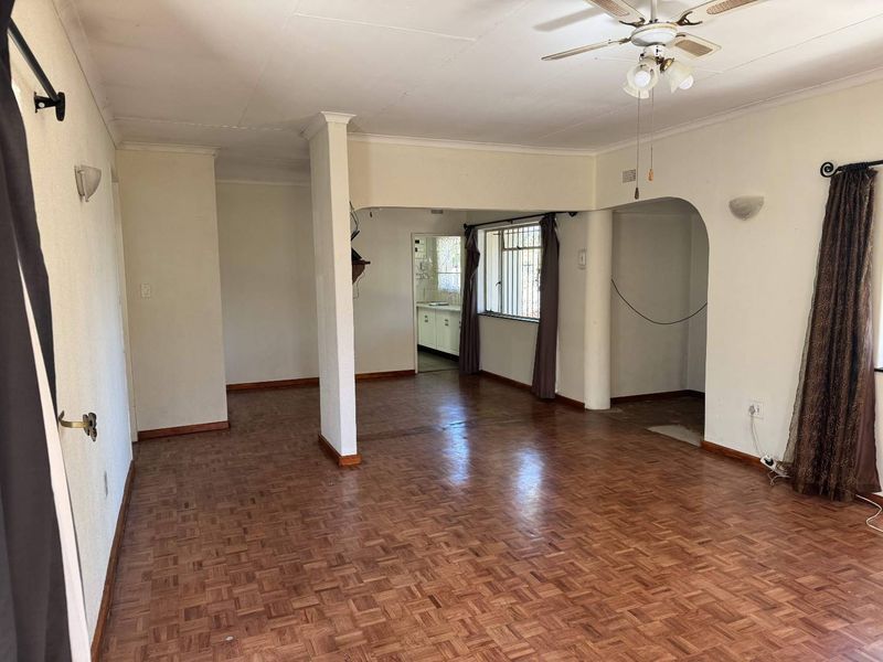 Spacious open-plan living area featuring traditional parquet flooring, a ceiling fan, and architectural archways leading to adjacent rooms.