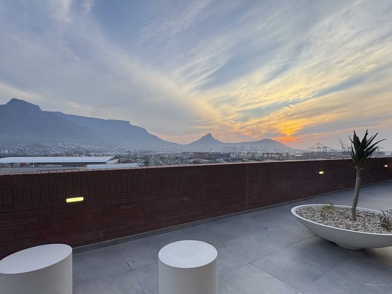 A modern balcony featuring tiled flooring, a brick parapet wall with integrated lighting, and expansive mountain and city views.