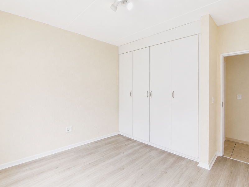 A bright, empty bedroom featuring neutral walls, modern laminate flooring, and ample built-in cupboard storage space.
