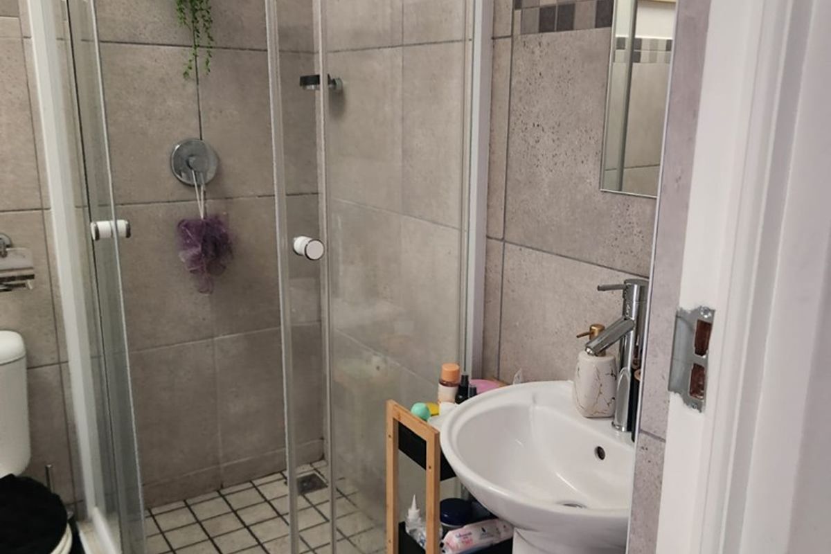 Compact bathroom featuring a glass shower enclosure, pedestal basin with mixer tap, and neutral wall and floor tiling.