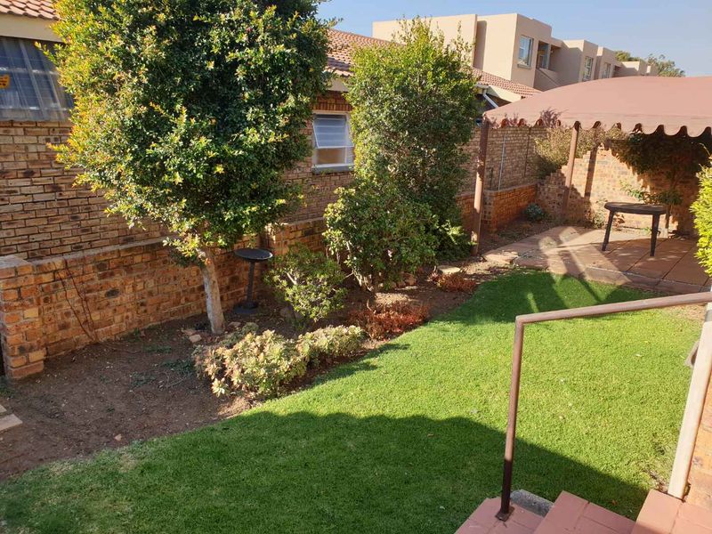 A private rear garden featuring a paved patio area with a fixed awning, established trees, and a brick boundary wall.