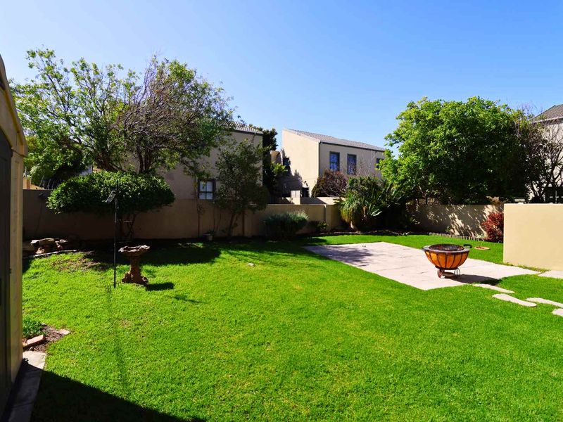 A well-maintained private garden featuring a lush green lawn, a paved patio area, and secure boundary walls.