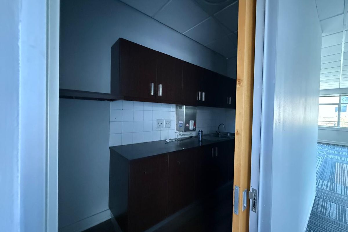 A compact office kitchenette featuring dark wood cabinetry, a tiled backsplash, and a stainless steel sink.