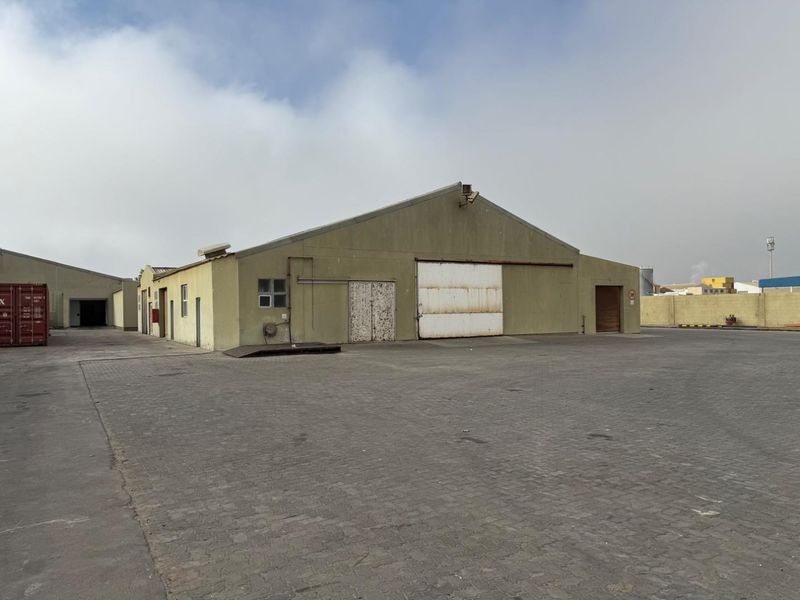 Industrial warehouse facility featuring a large paved yard, gabled roof structure, and multiple sliding access doors for logistics and storage operations.