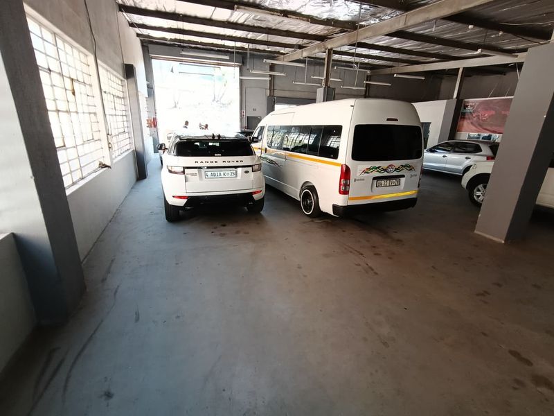 Spacious industrial garage featuring exposed steel roof trusses, concrete flooring, and large steel-framed windows, suitable for vehicle storage or workshop use.
