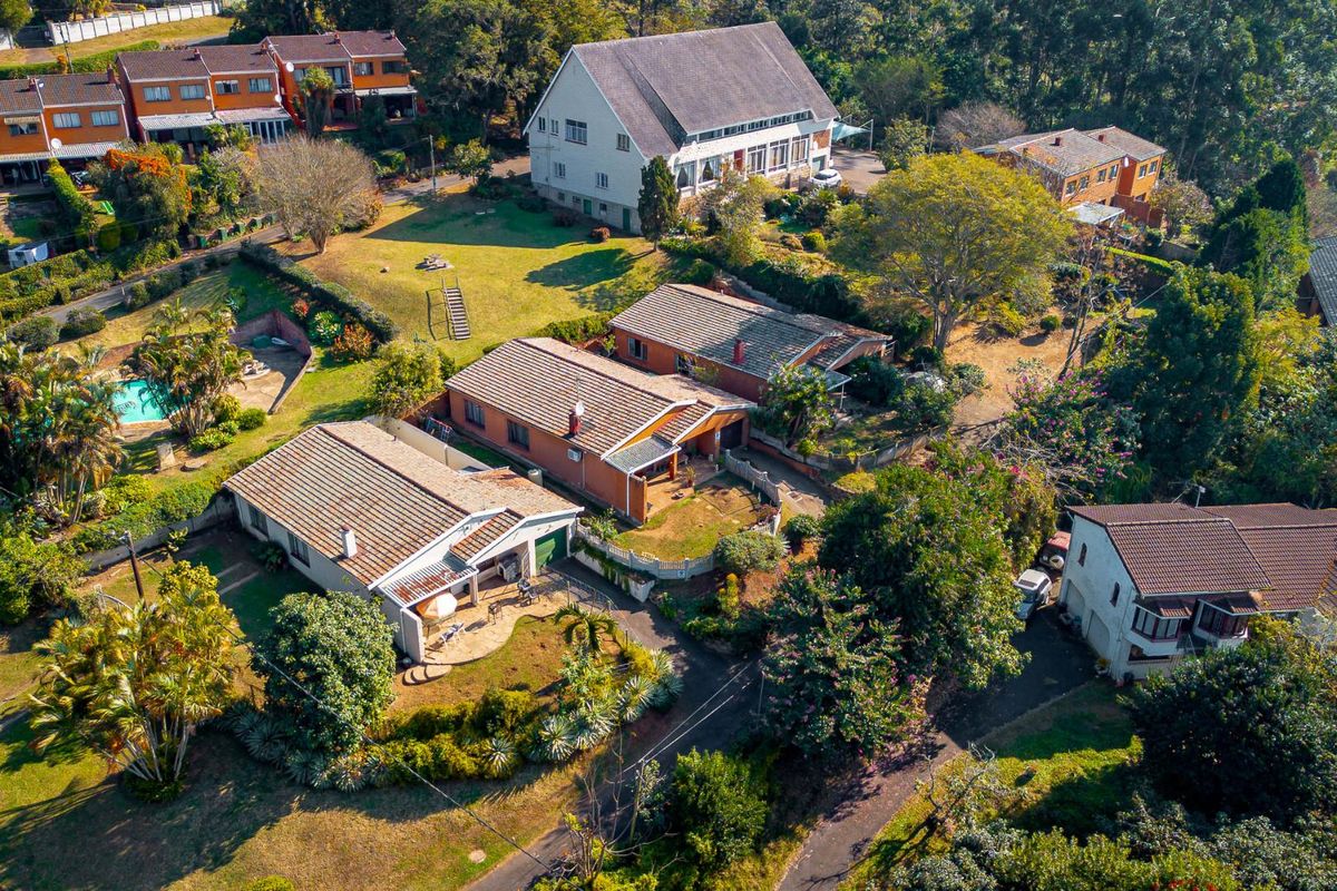 An aerial view of a residential townhouse complex featuring multiple units with tiled roofs, established gardens, and a communal swimming pool area.