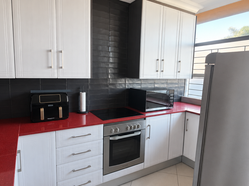 A modern kitchen featuring white cabinetry, striking red countertops, a black subway tile backsplash, and integrated stainless steel oven and cooktop.