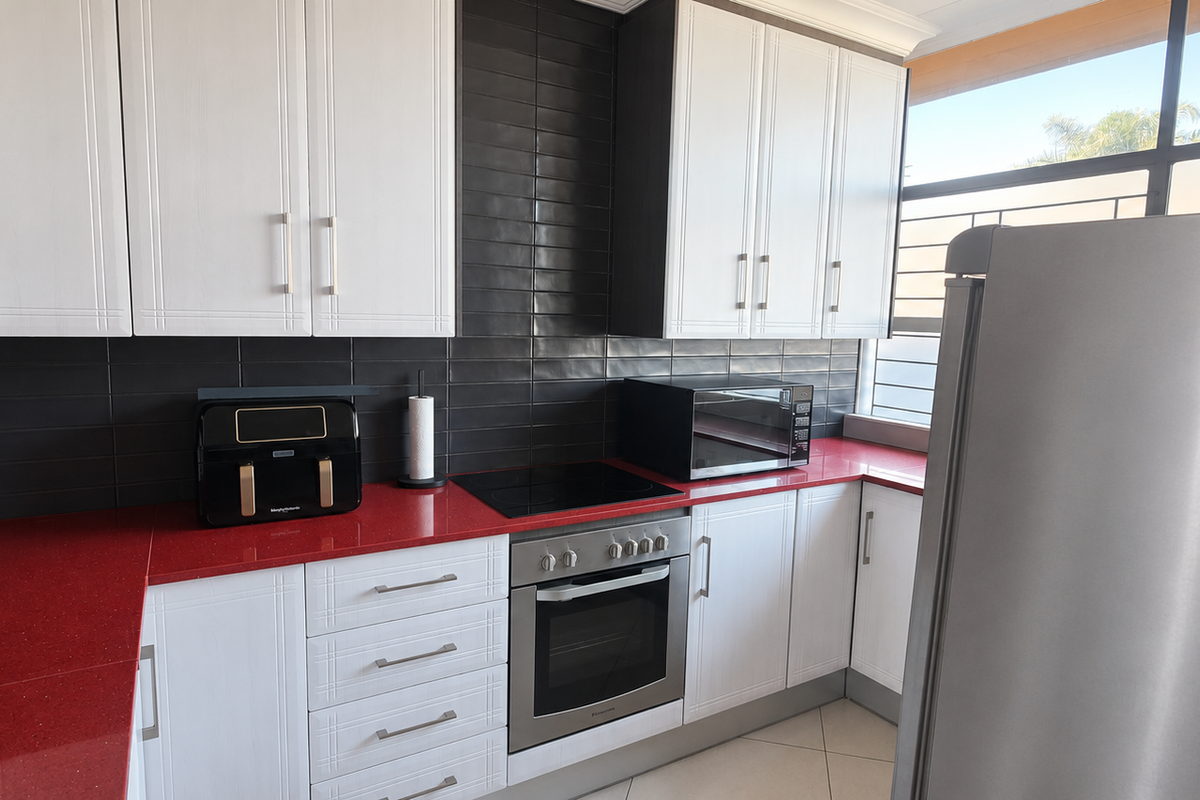 A modern kitchen featuring white cabinetry, striking red countertops, a black subway tile backsplash, and integrated stainless steel oven and cooktop.