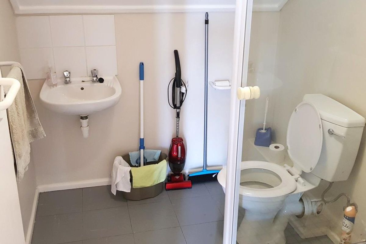 A compact office bathroom featuring a wall-mounted basin, tiled splashback, and a standard toilet suite with tiled flooring.