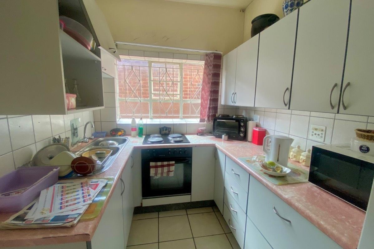 A compact kitchen featuring white cabinetry, laminate countertops, a built-in oven and hob, and tiled flooring with a security-barred window.