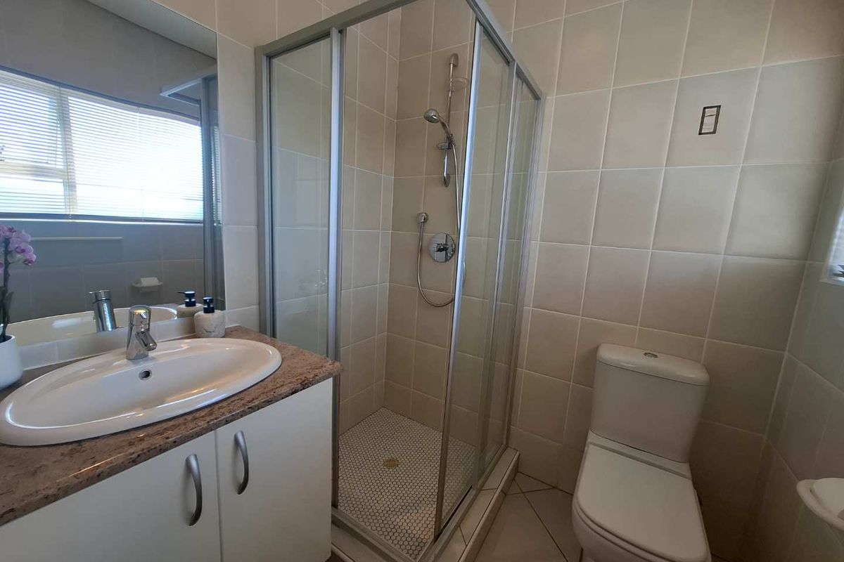 A functional bathroom featuring a corner shower enclosure, a vanity with a basin, and a toilet, finished with neutral wall and floor tiling.