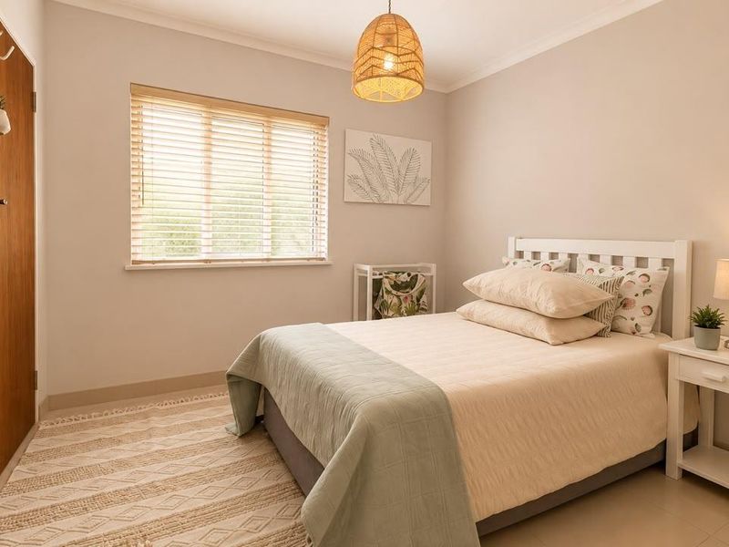 A well-maintained bedroom featuring neutral walls, tiled flooring, a built-in wardrobe, and natural light through venetian blinds.