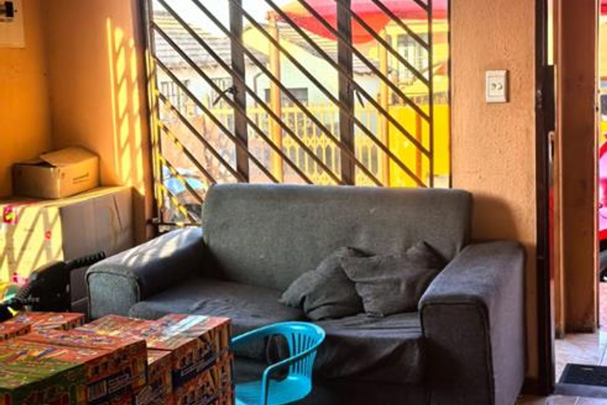 A living room featuring a decorative ceiling rose, chandelier, and security bars on the window, with tiled flooring throughout.