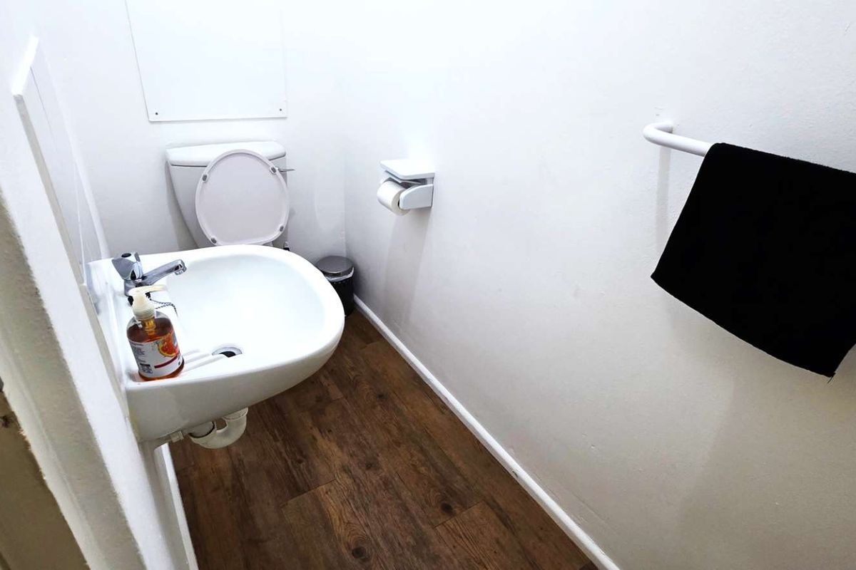 A compact office restroom featuring a wall-mounted basin, toilet, and wood-look flooring.