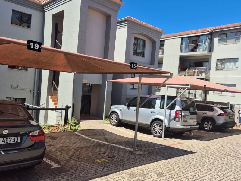 Exterior view of the apartment complex featuring designated covered parking bays and multi-story residential units with balconies.