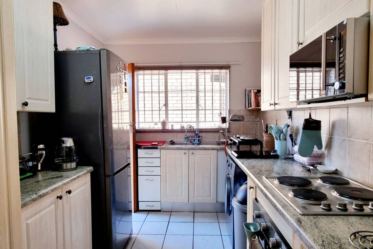 A functional kitchen featuring light-toned cabinetry, granite-look laminate countertops, a built-in oven and hob, and tiled flooring with a window overlooking the exterior.