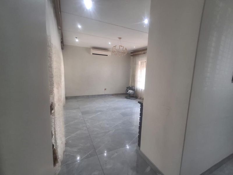 A bright, open-plan living area featuring large format grey floor tiles, recessed downlighting, and a wall-mounted split-system air conditioner.