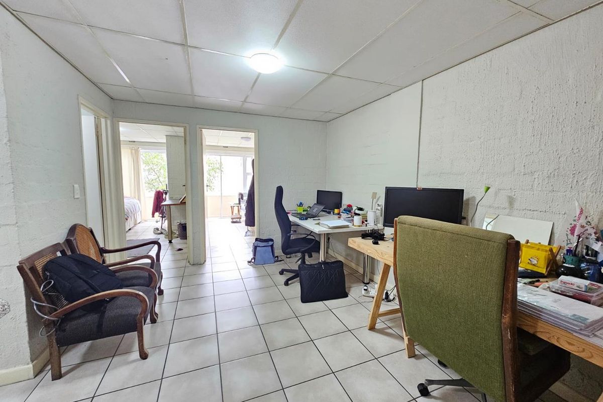 A multi-purpose living area featuring tiled flooring and a drop ceiling, currently utilized as a home office space with access to adjacent rooms.
