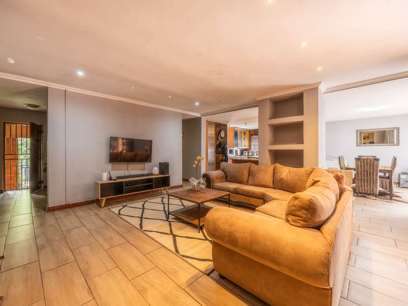 Spacious open-plan living area featuring tiled flooring, recessed lighting, and a built-in shelving unit, seamlessly connecting to the dining and kitchen spaces.