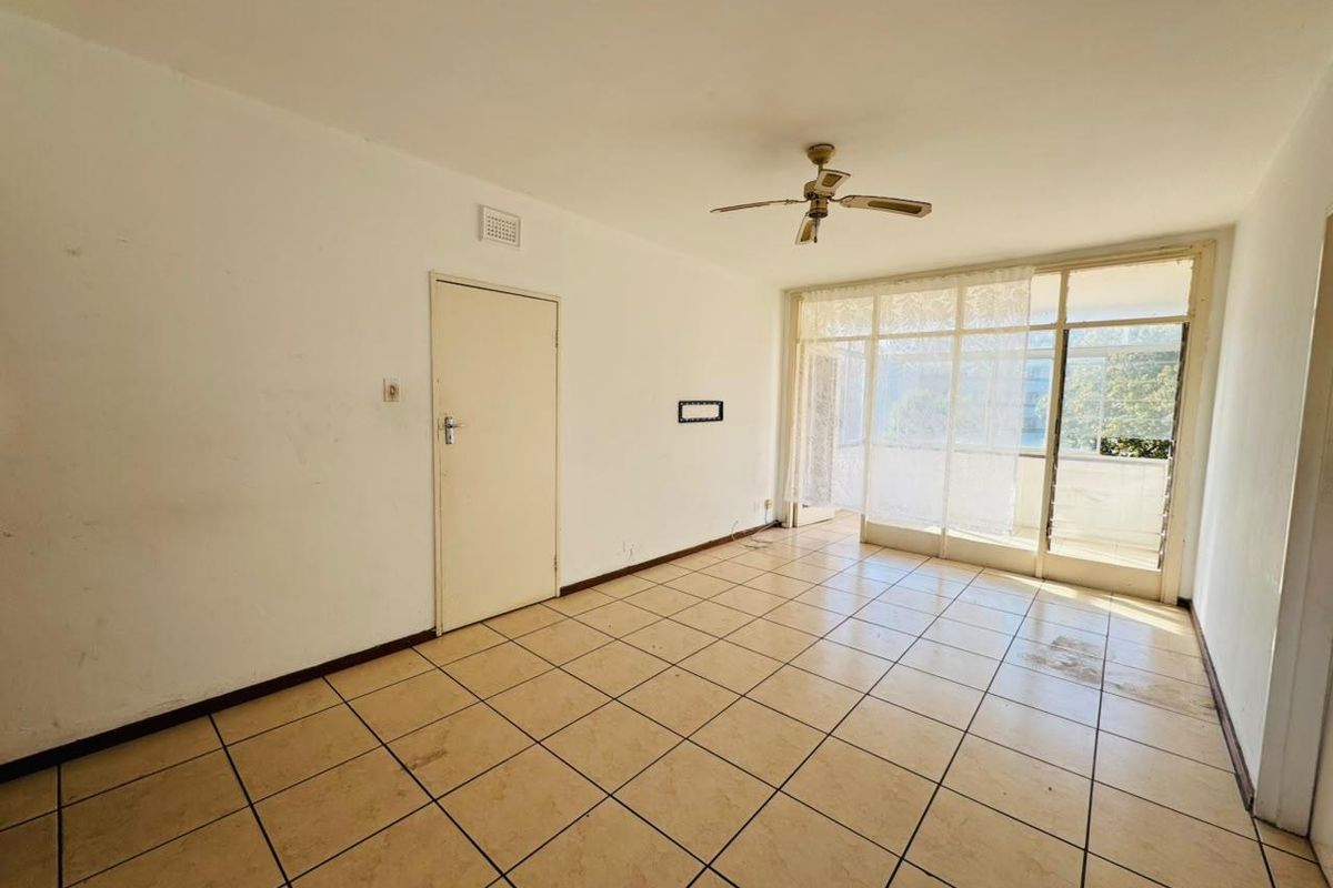 An empty, sunlit living area featuring tiled flooring, a ceiling fan, and large sliding glass doors leading to an outdoor space.
